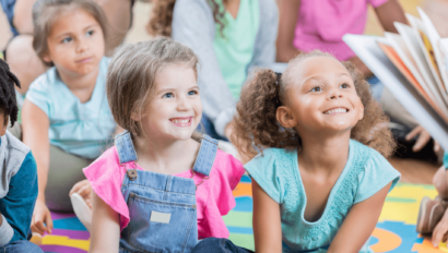 Two little girls smiling as someone reads a story to them.
